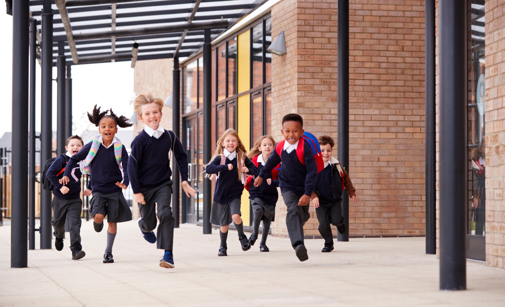Primary school kids, wearing school uniforms and backpacks, running on a walkway